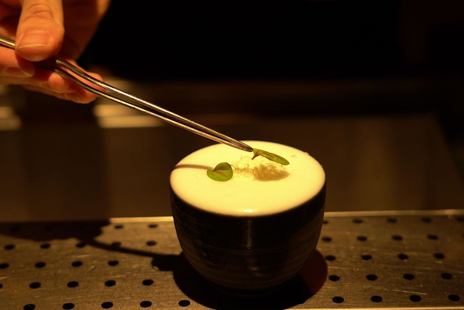 Bartender creating coffee art using chopsticks to draw shapes in a dark cup with foamy latte.
