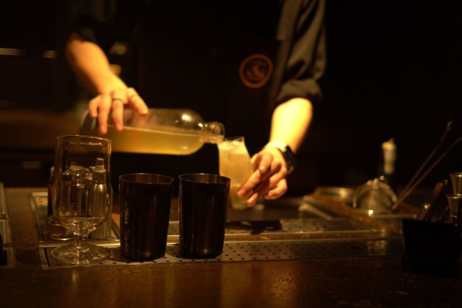 Hands pouring drinks behind dimly lit bar counter.
