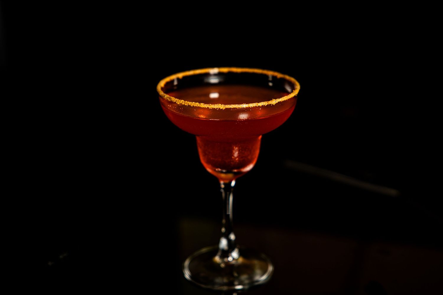 A classic margarita cocktail with a gold rim glows in dramatic lighting against a dark background.
