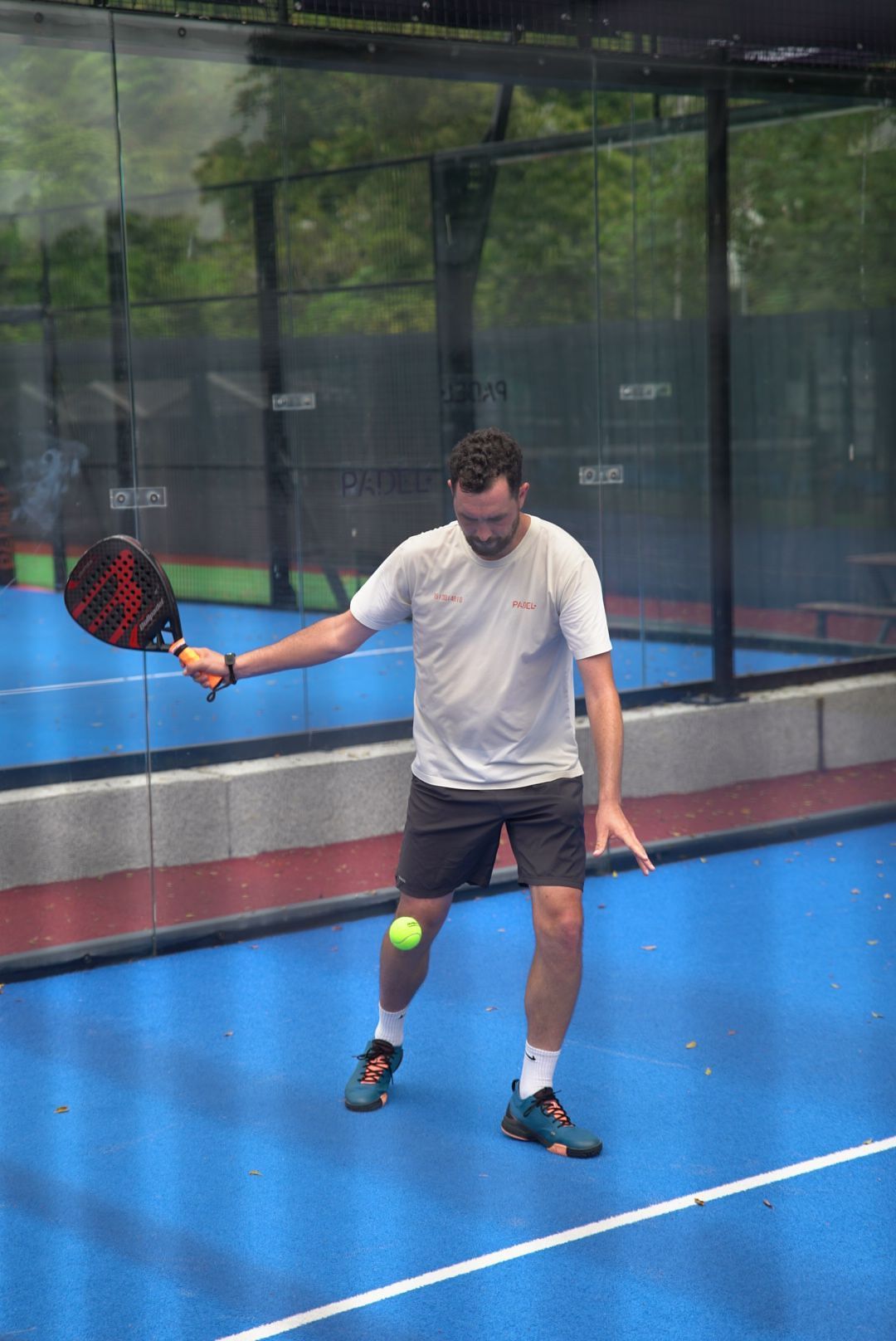 Player on blue paddle tennis court demonstrating ball control technique with red paddle during game.