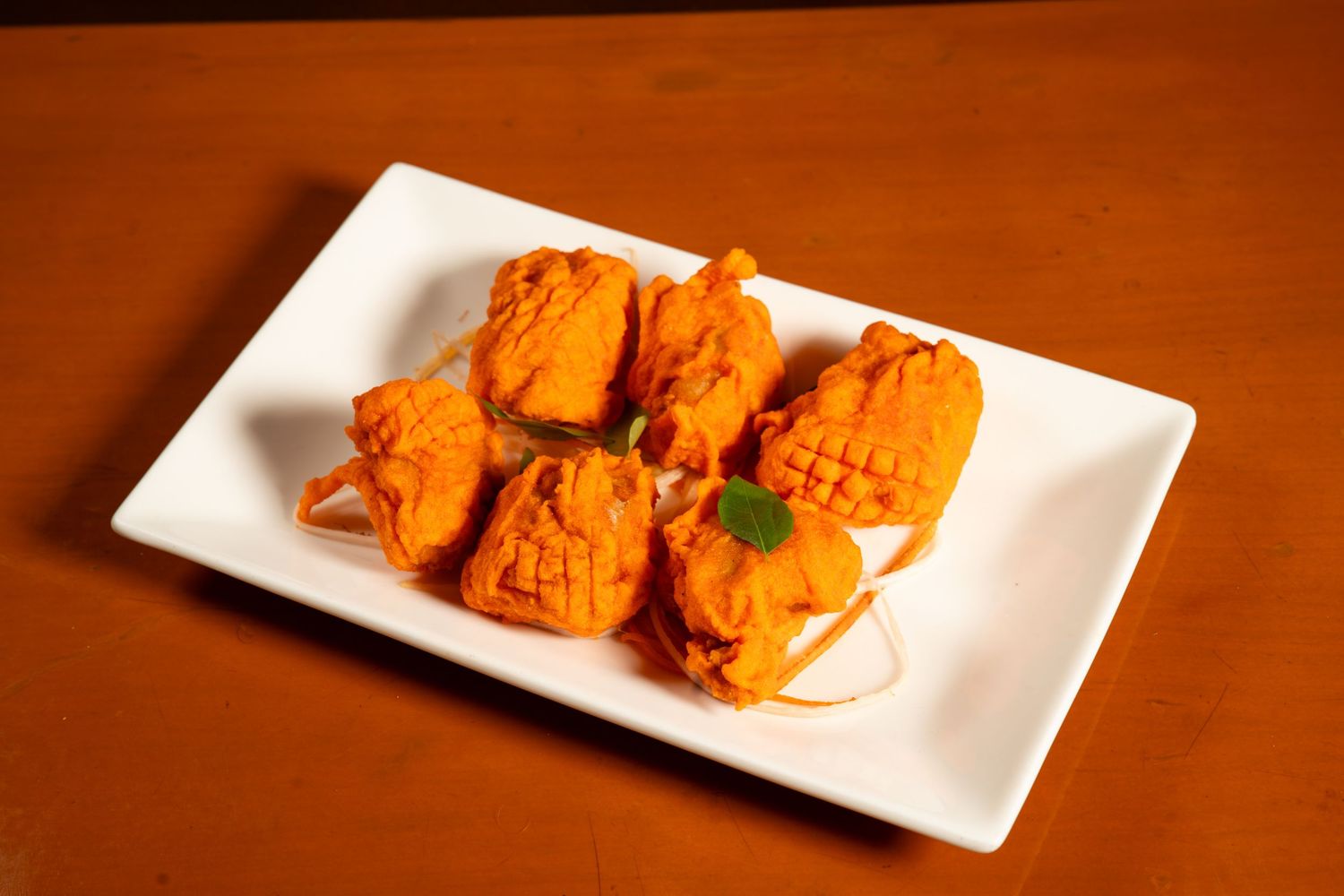 Orange colored Indian paneer tikka appetizers served on a white rectangular plate against a wooden background.