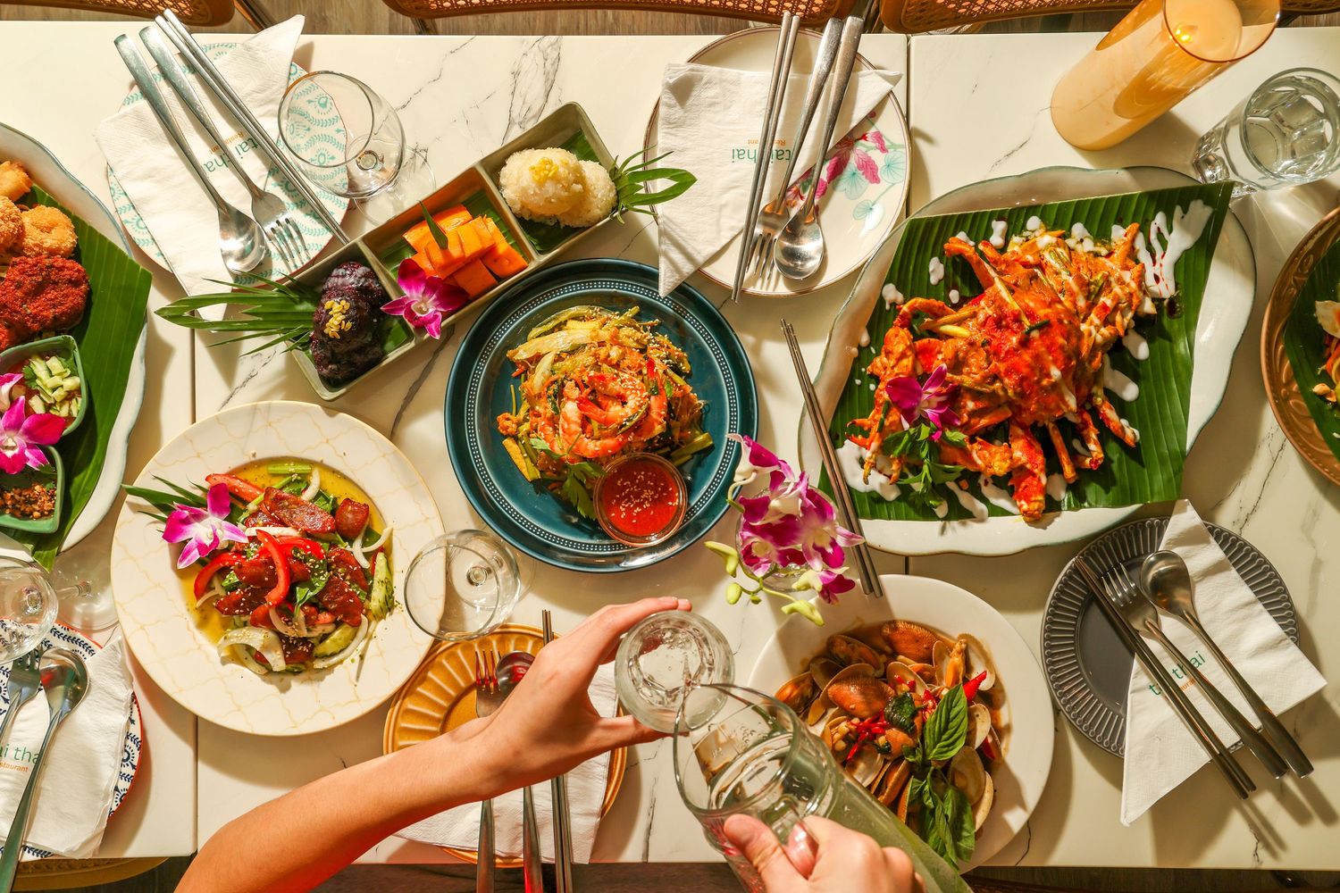 Overhead view of colorful Thai dishes served on a table with orchid flowers and banana leaves as garnish.
