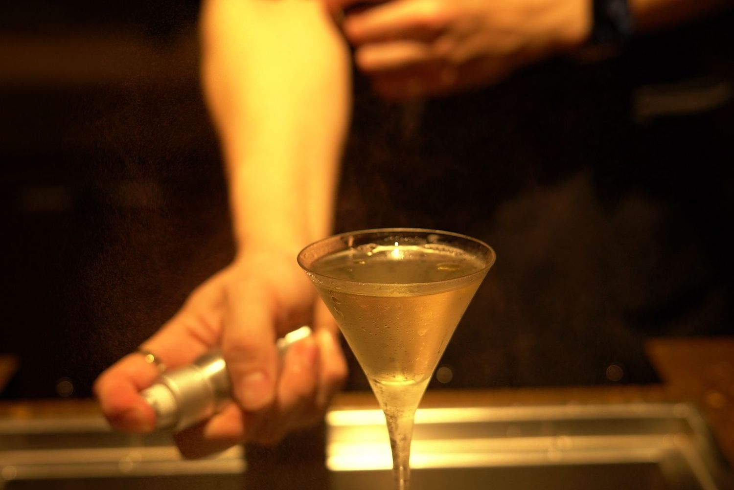Martini glass being garnished at a dimly lit cocktail bar.