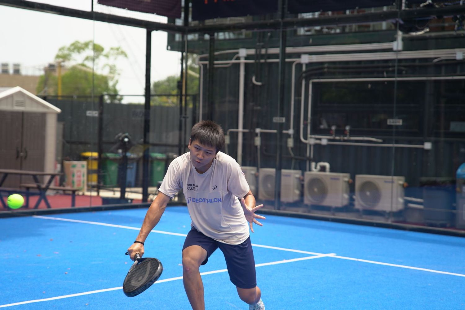 Player in defensive stance preparing to return a shot on blue padel court.