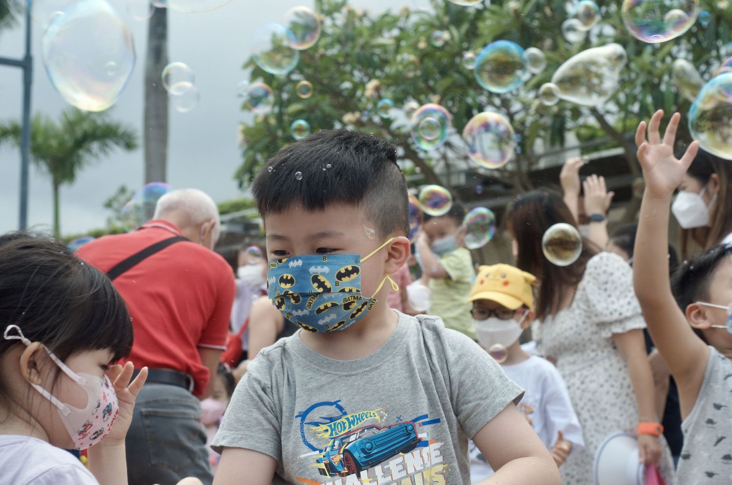 People enjoying an outdoor bubble show in front of trees.