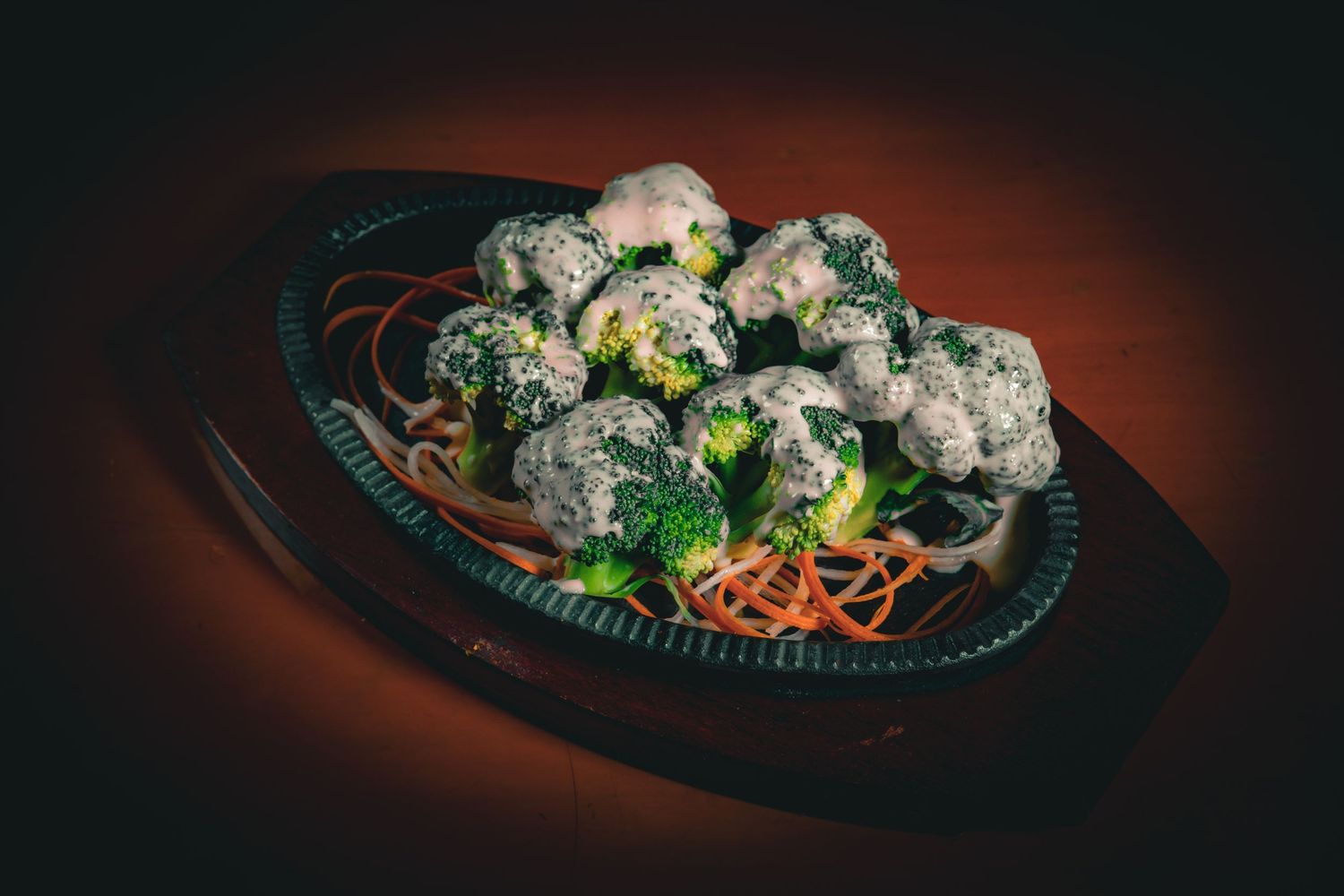 Steaming hot sizzling platter with meatballs, broccoli and noodles served on a dark cast iron plate.