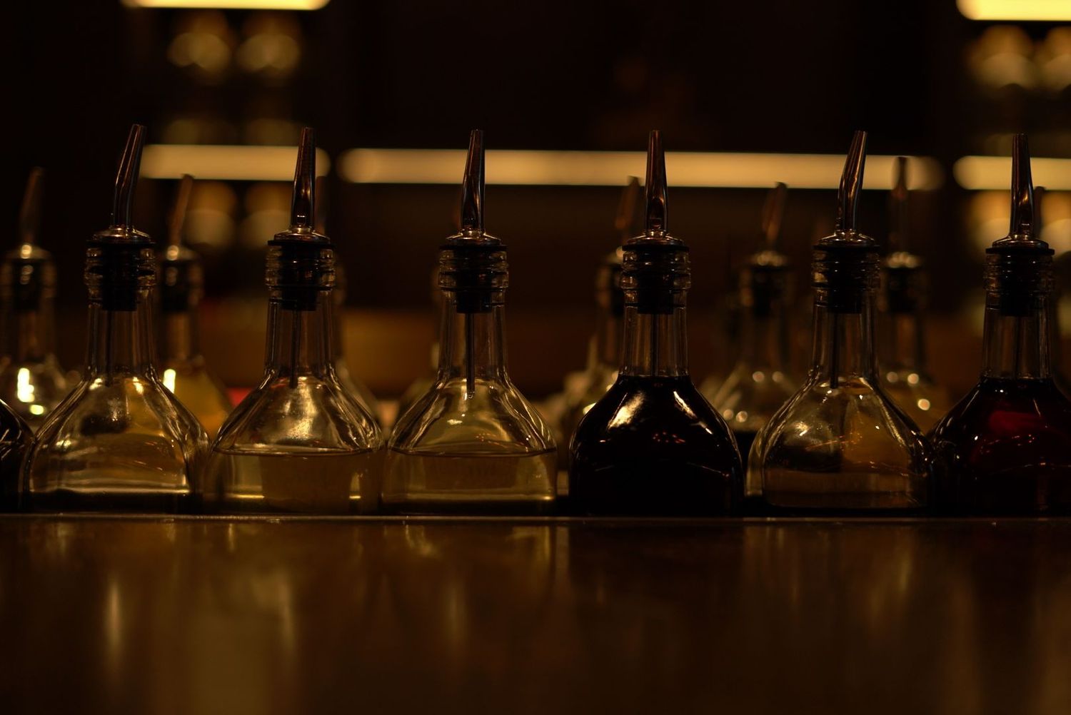Row of backlit wine bottles arranged on dark wooden shelf.