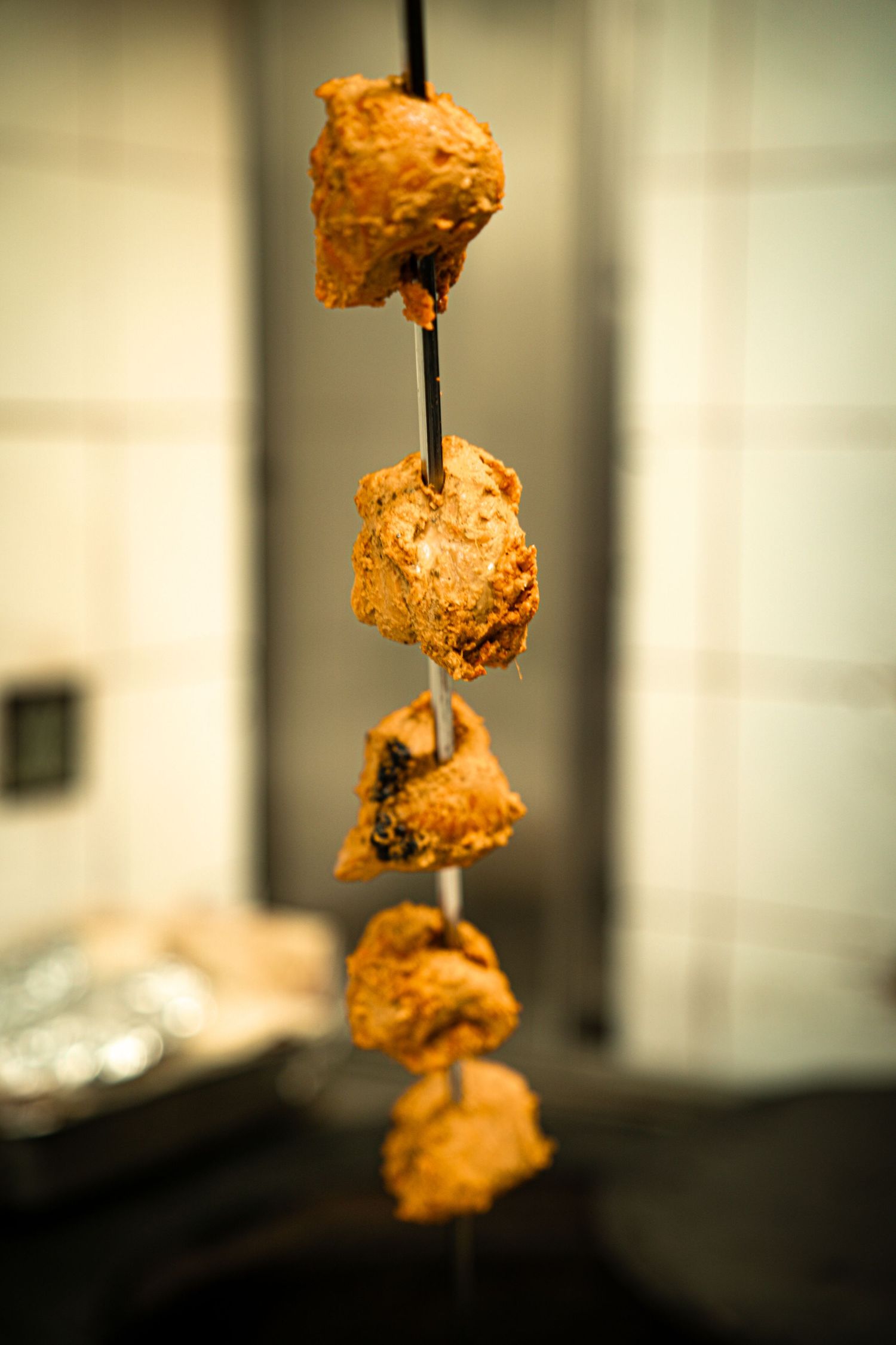 Five breaded chicken pieces stacked vertically on a metal skewer against a blurred background.