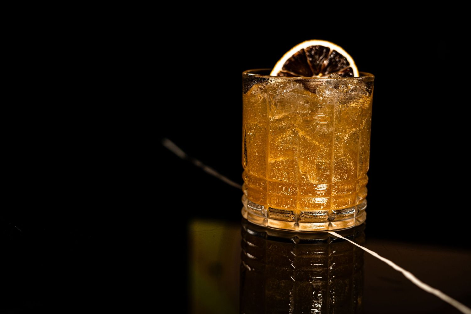 Classic cocktail with citrus wheel garnish in rocks glass reflecting on dark surface.