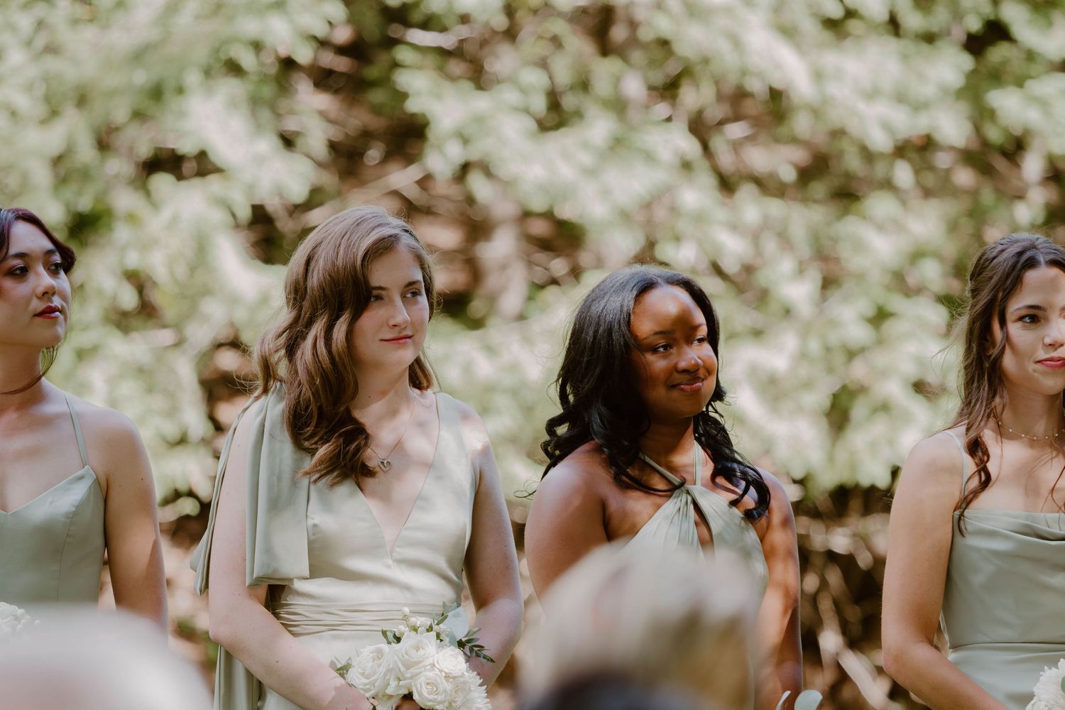 Bridesmaids in coordinated dresses stand together during an outdoor wedding ceremony.