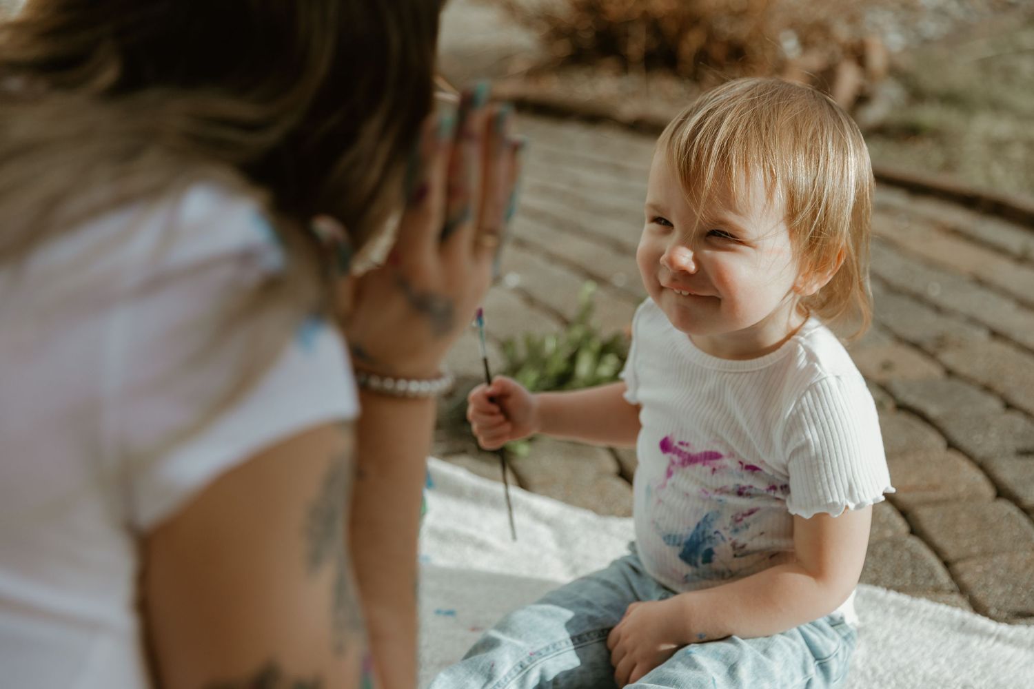 A young toddler shares a playful moment while holding a small stick on an outdoor deck.