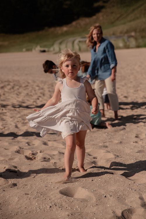 A child in a flowing white dress twirling on the beach sand.