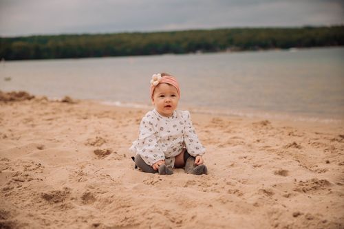 Baby crawling on sandy beach near water's edge.