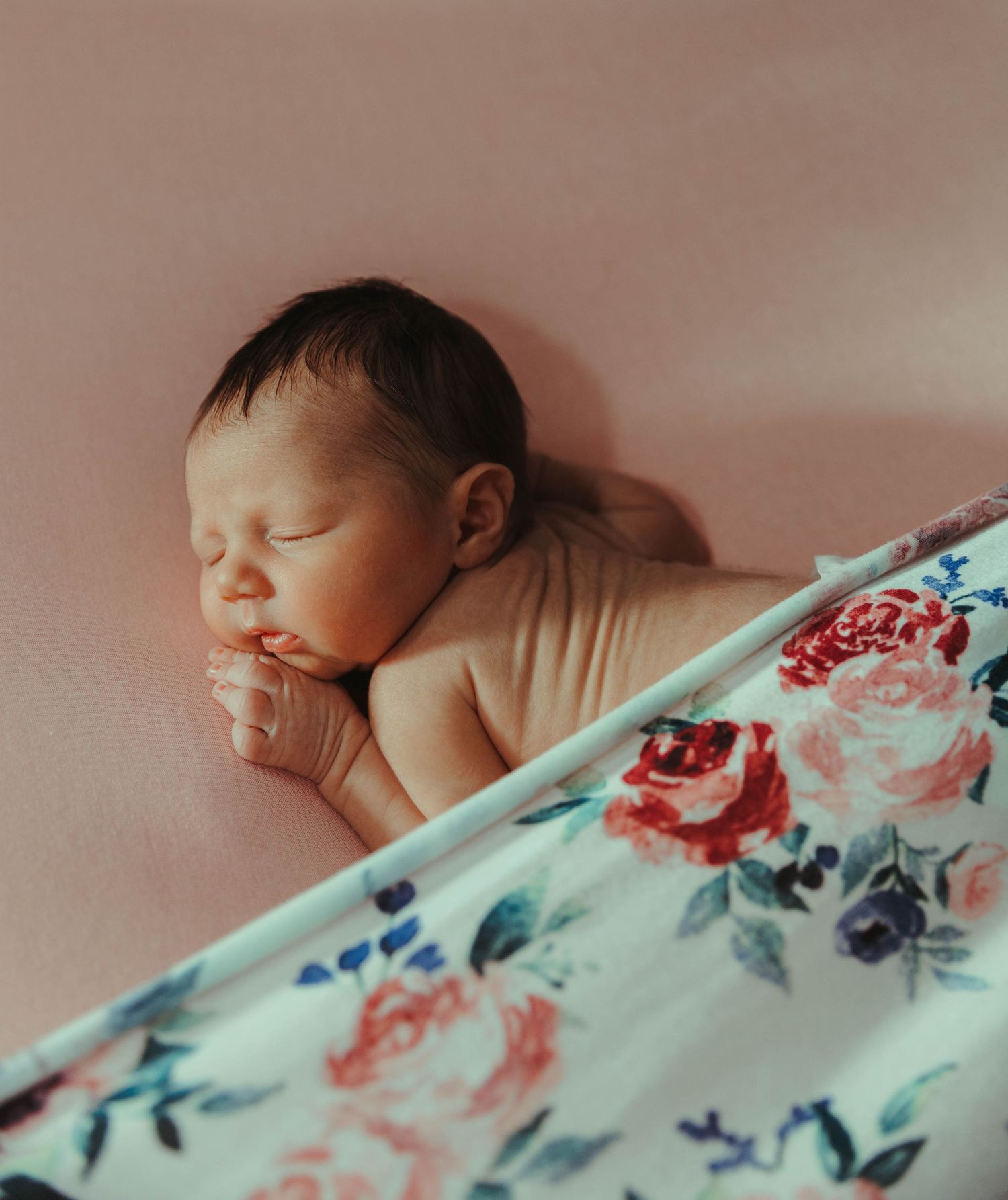 A sleeping newborn baby lies peacefully on soft bedding next to a turquoise floral patterned blanket.