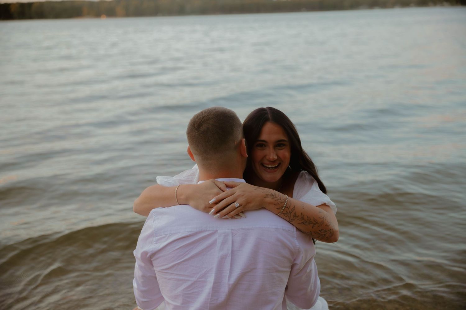 People in white outfits embracing on a beach with water in the background.