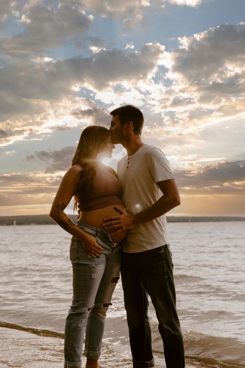 A silhouetted couple embraces on a beach at sunset with dramatic cloudy skies.