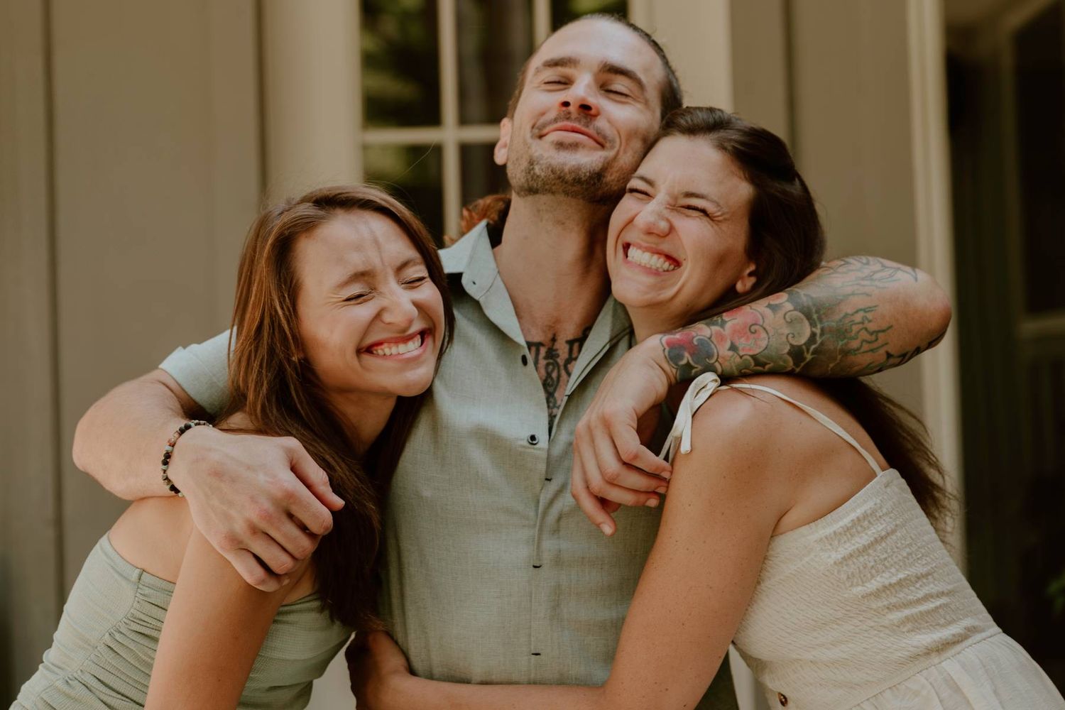 Three friends laughing and hugging outdoors in a joyful candid moment.