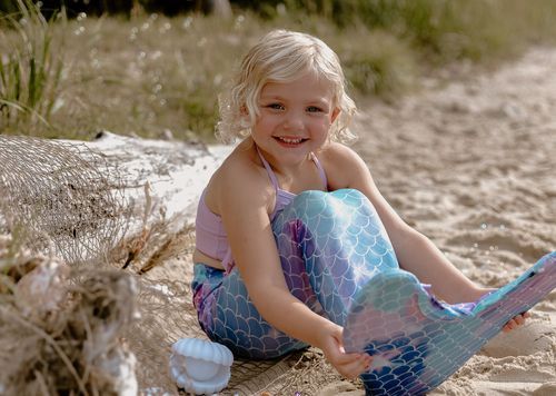 Coastal portrait featuring iridescent mermaid tail costume and natural beach setting.