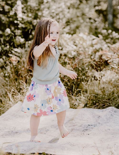 Dancing barefoot in a meadow wearing a floral skirt on a sunny summer day.