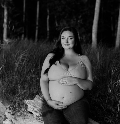 Black and white maternity portrait in natural woodland setting.