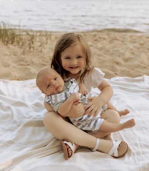 Sweet family beach portrait on white blanket with beachwear and sand in background.