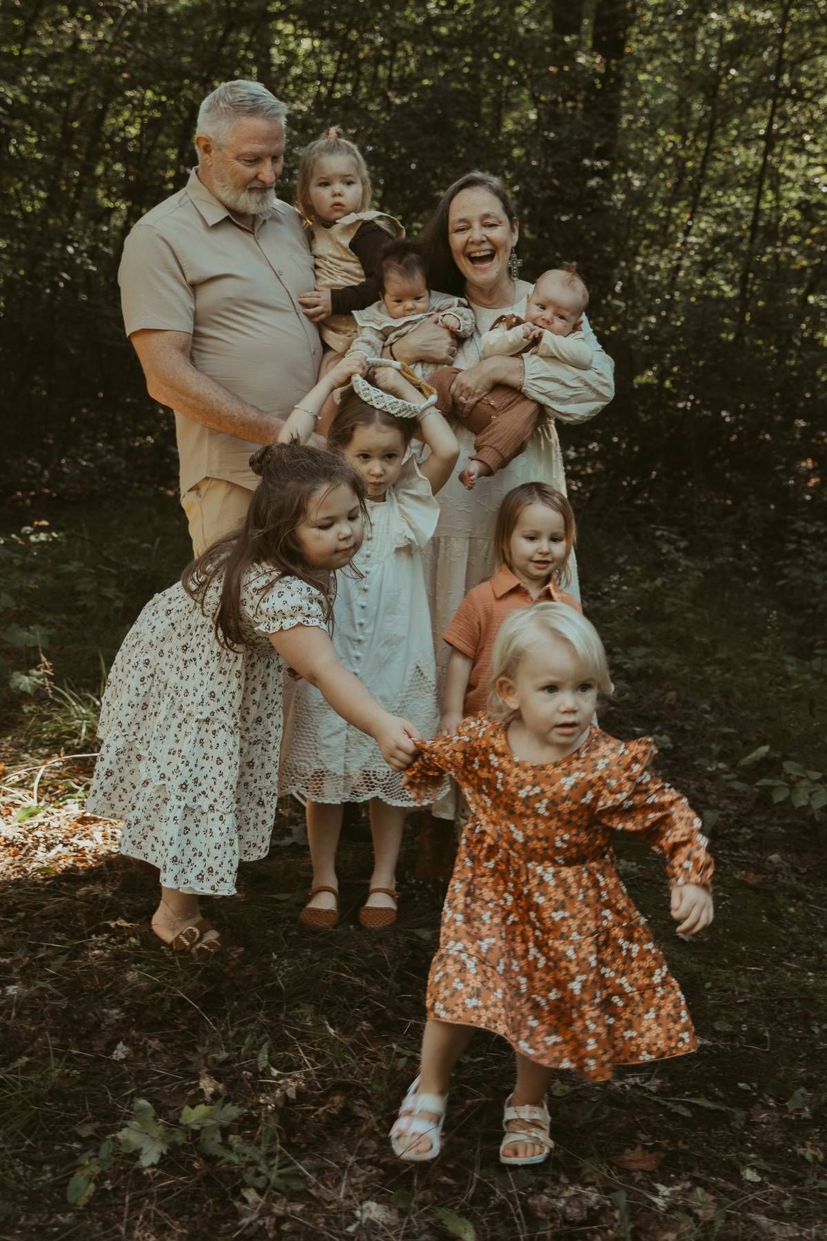 Large family portrait with parents and six young children posing outdoors in a lush green forest setting.
