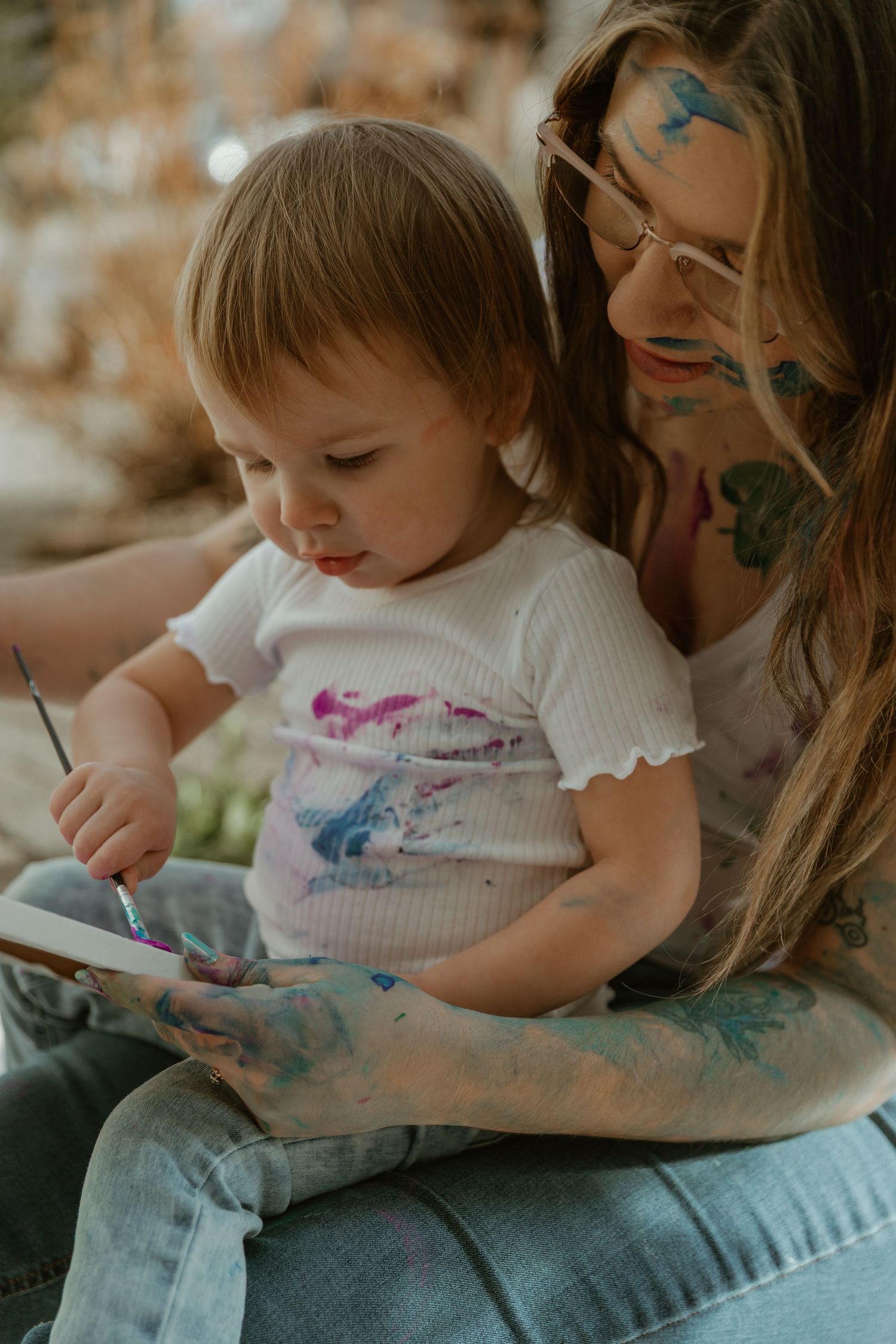 A child wearing a white shirt sits on someone's lap looking at a book together in warm sepia tones.