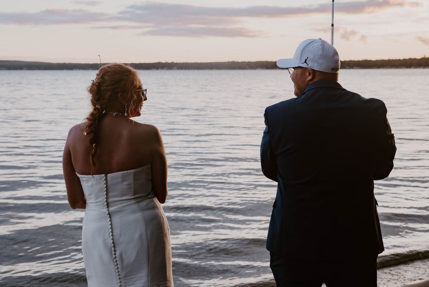 A couple sits together on a bench watching a sunset over the ocean.