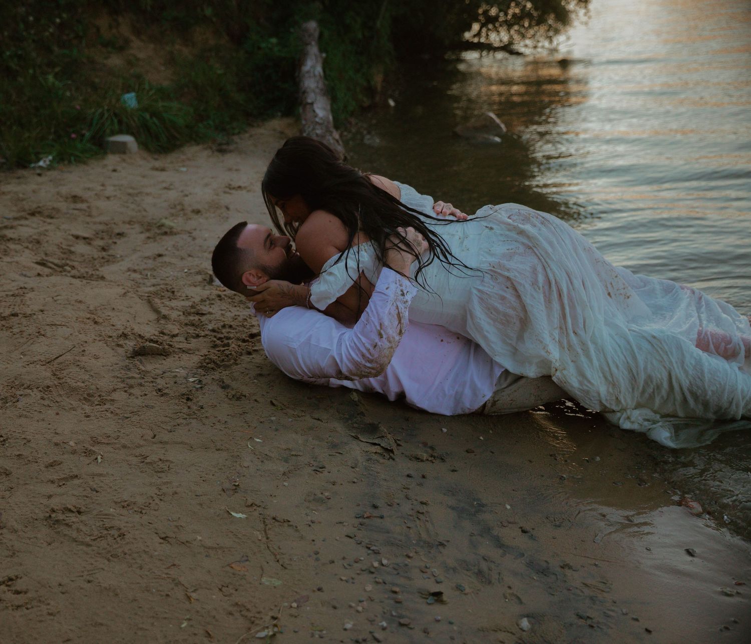 Romantic couple dressed in white sharing intimate moments on a beach at dusk.