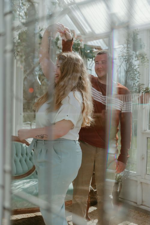A couple dancing together in a sunlit conservatory with white decor and greenery.