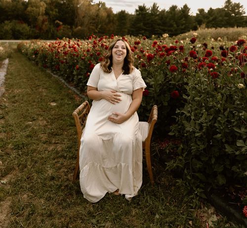 A person in a white dress sits joyfully on a chair surrounded by rows of red poppies.
