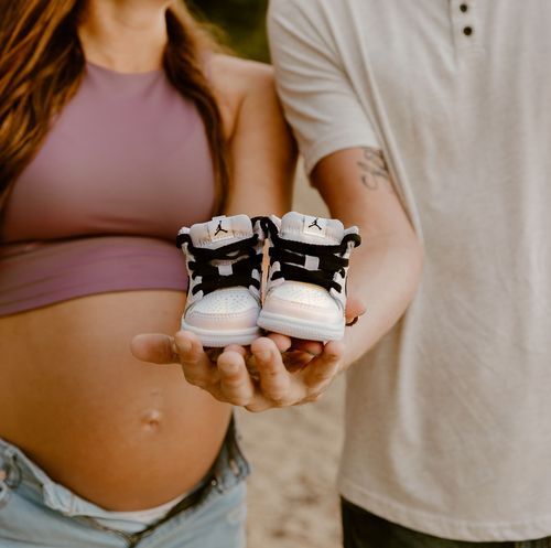 Small black and white baby sneakers held in hands against backdrop of beach setting.
