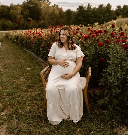 A figure in white sits on a wooden chair amid rows of red poppies in a garden setting.