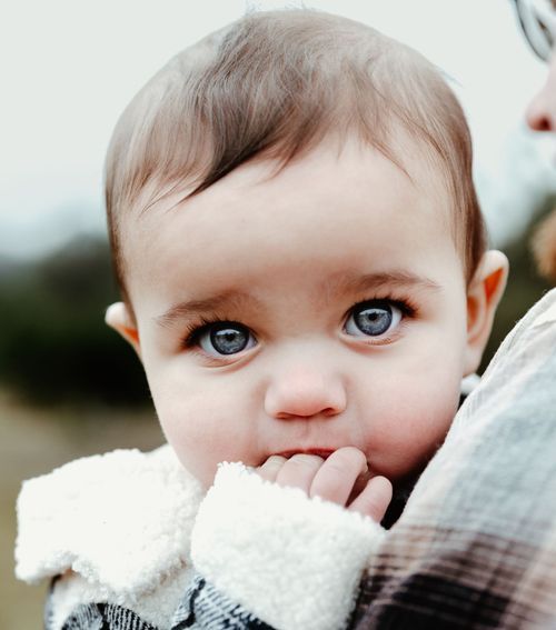 A young child wearing cozy winter clothing looks at the camera with bright blue eyes.