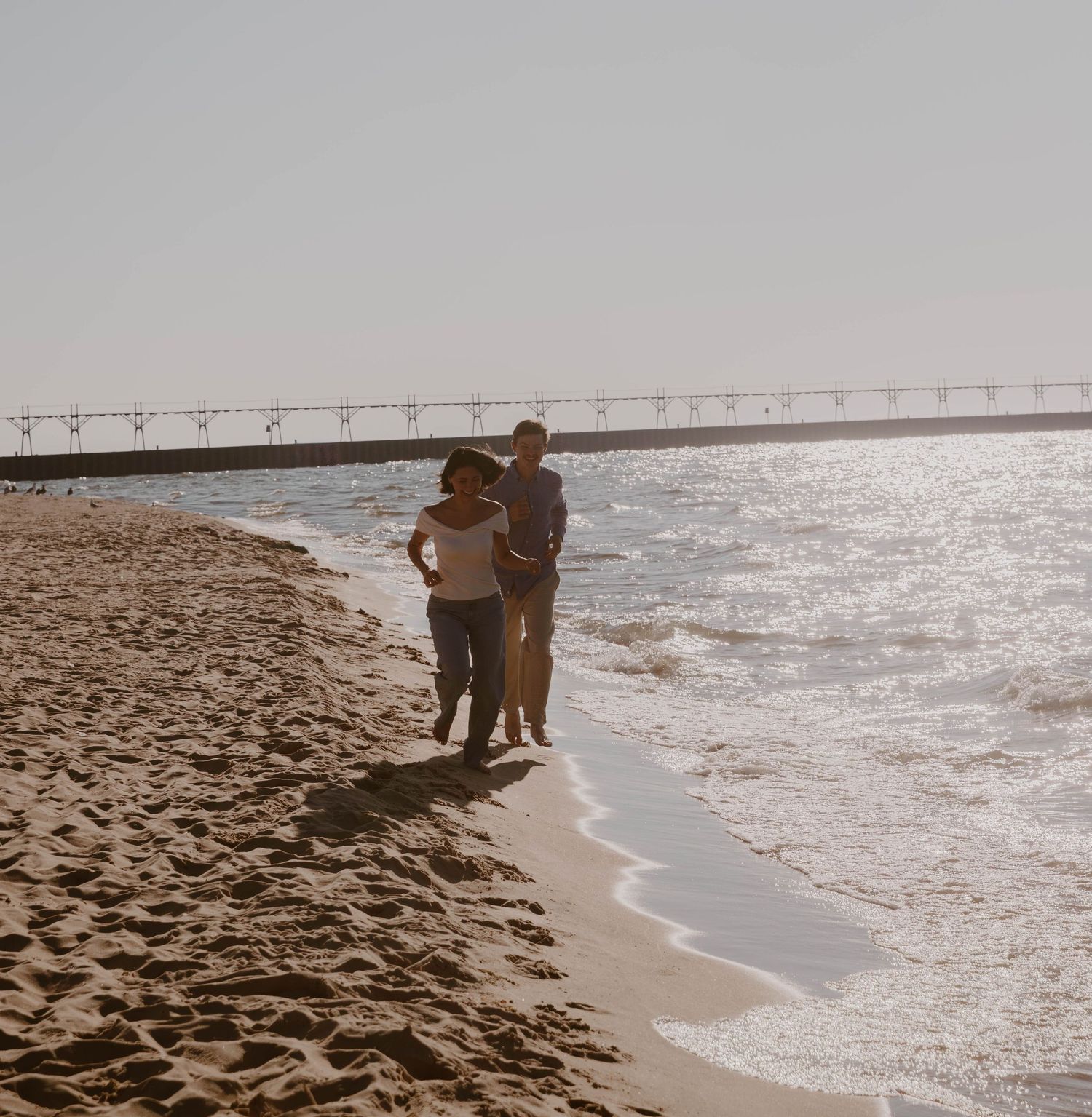 Silhouettes of people walking along a sandy beach shoreline at sunset with gentle waves rolling in.
