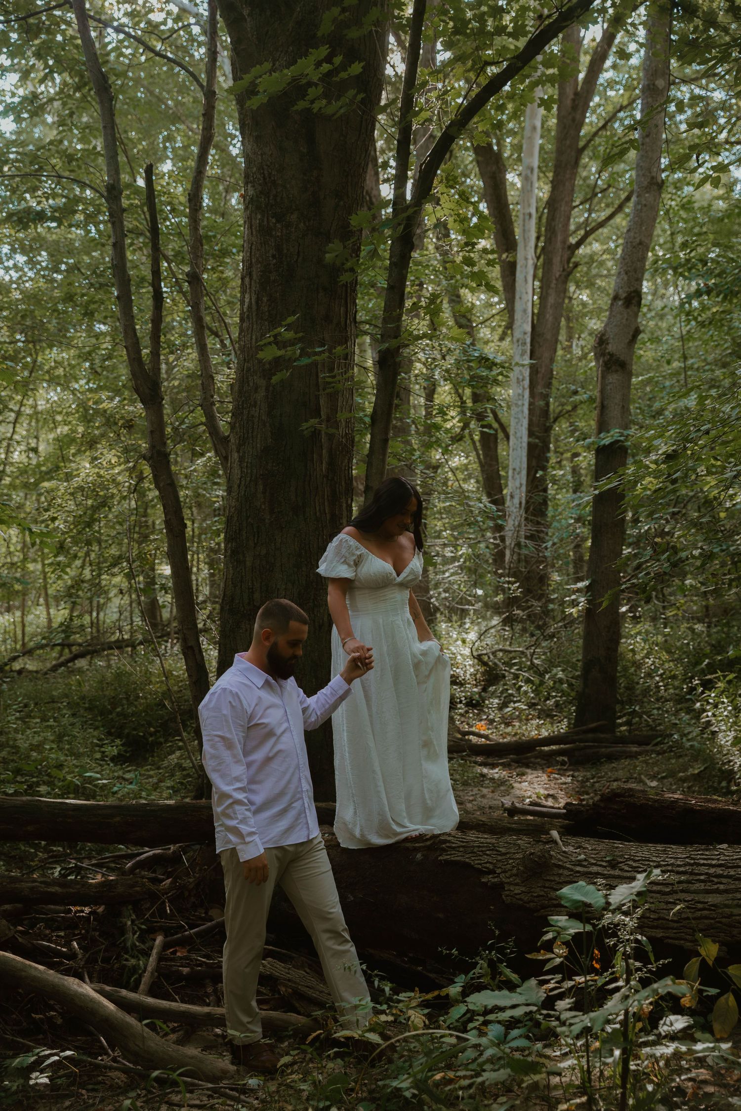 A couple shares a tender moment in a lush green forest setting during what appears to be an engagement photo session.