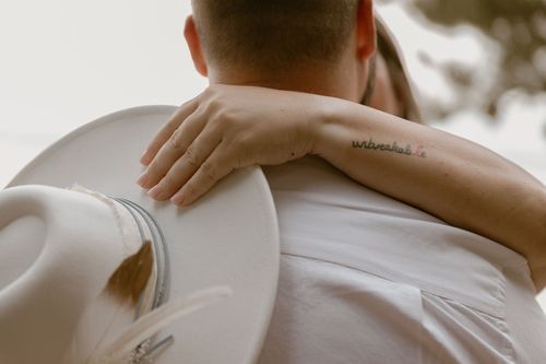 Close-up detail shot of hands and arms embracing against white formal attire.