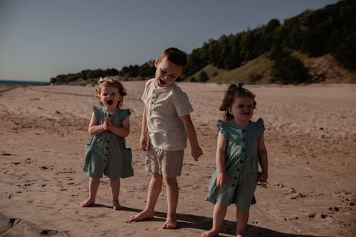 Three children playing together on a sandy beach during a sunny day.