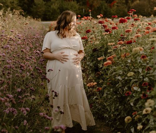 A person in a white dress poses among blooming red poppies and purple flowers in a garden.