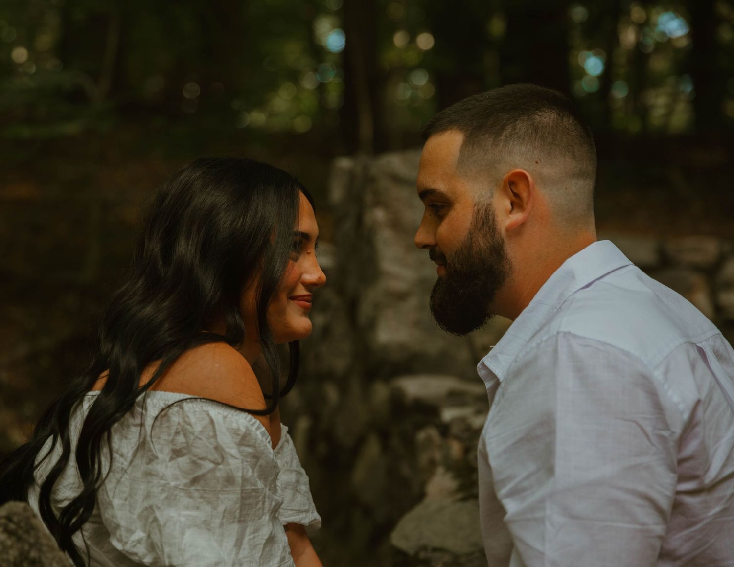 Romantic couple shares intimate moments in a wooded area during golden hour.