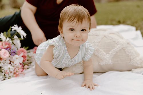 Baby crawling on white blanket next to pink flowers.