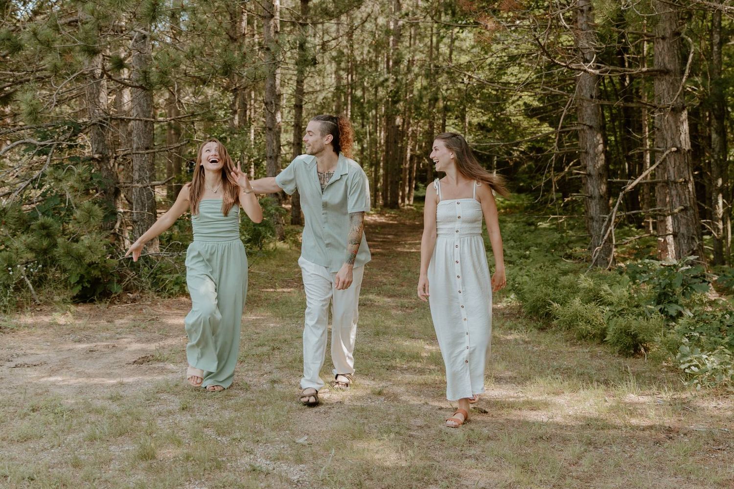 Three people in matching sage green outfits walking and laughing together on a forest path.