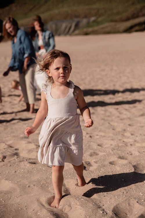 A child in a white dress running across beach sand at sunset.