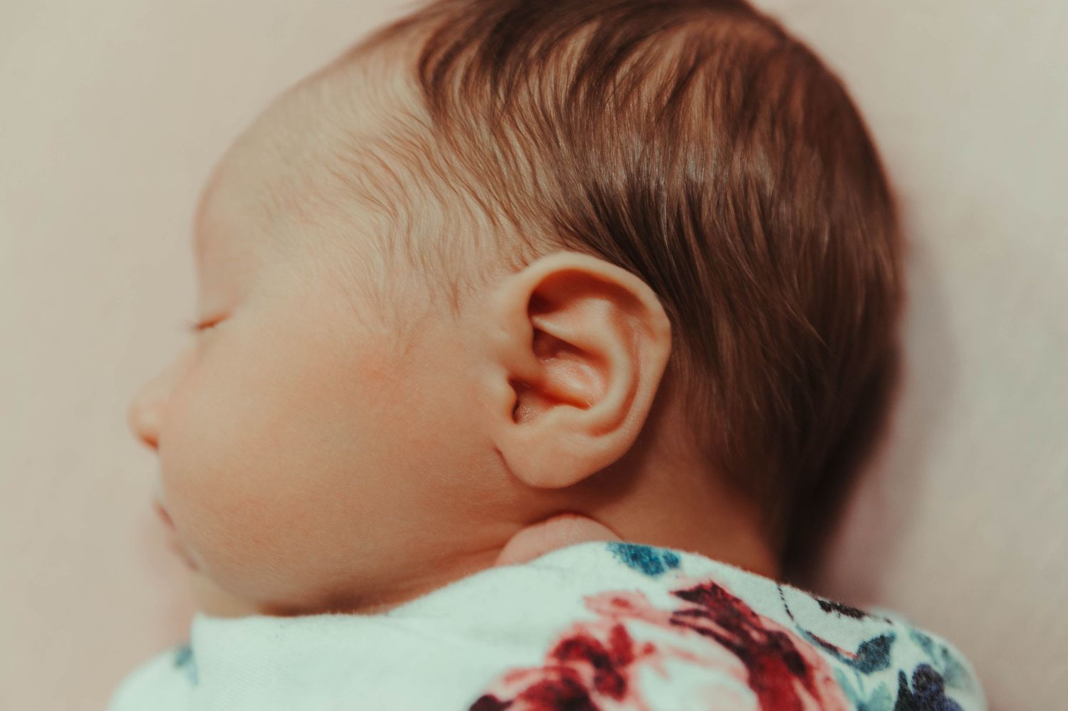 Close-up profile view of a sleeping baby with light brown hair wearing a floral print outfit.