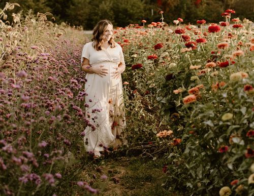 A figure in a flowing white dress walks through a garden of red poppies and purple wildflowers.