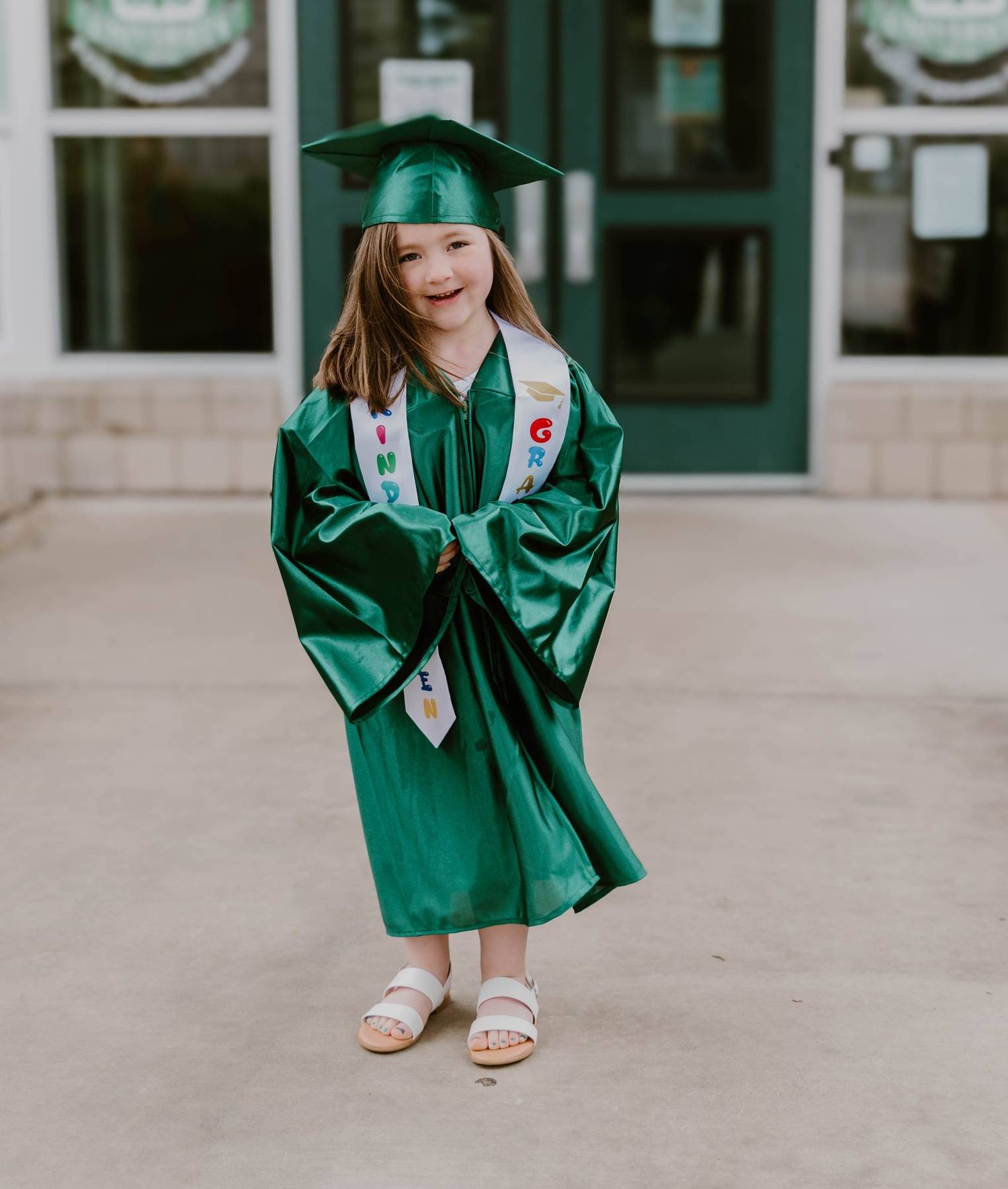 Graduate wearing emerald green cap and gown poses for photos during graduation ceremony outdoors.