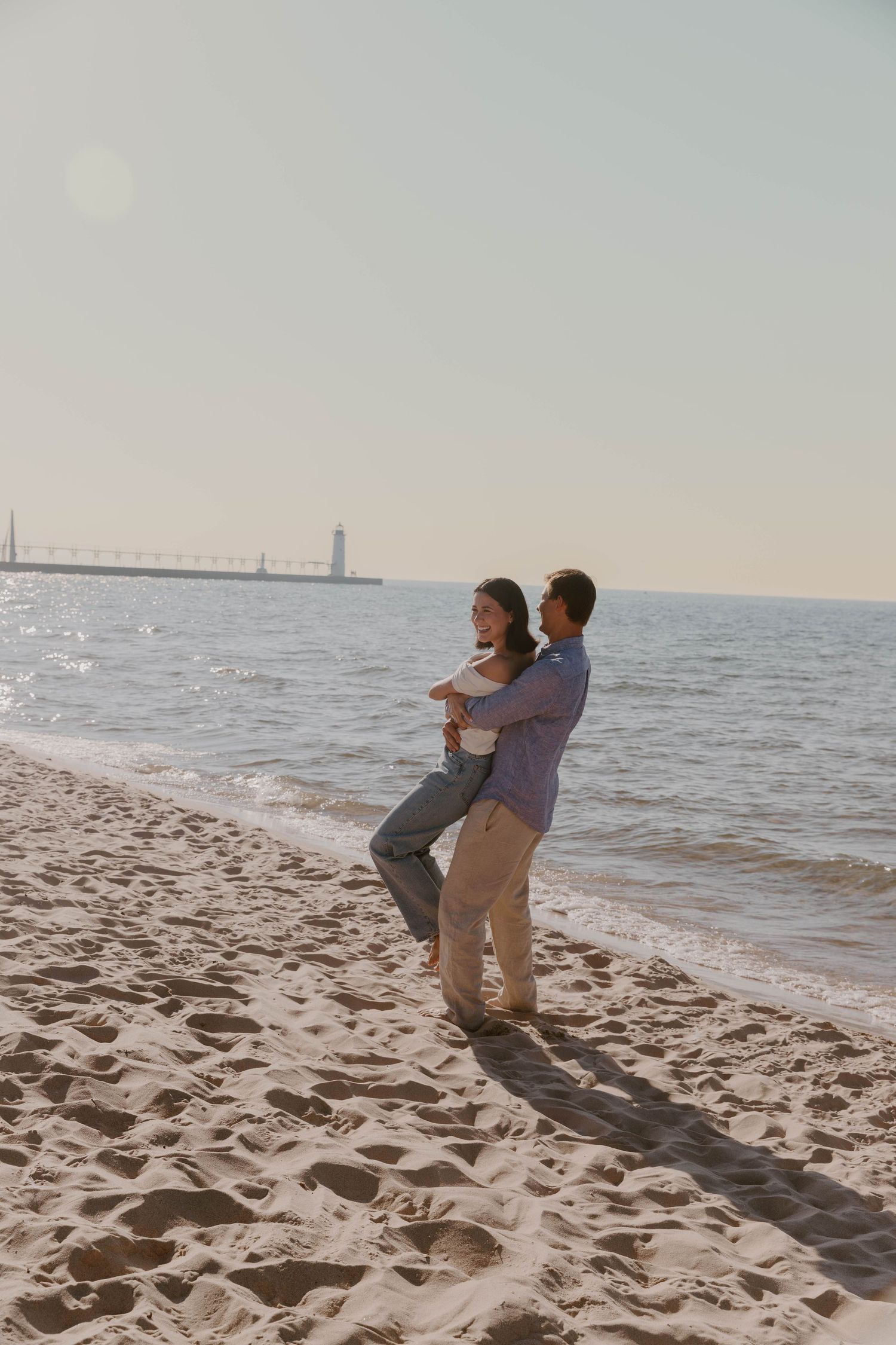 Playful couple dancing together on a sunny beach with ocean waves in the background.