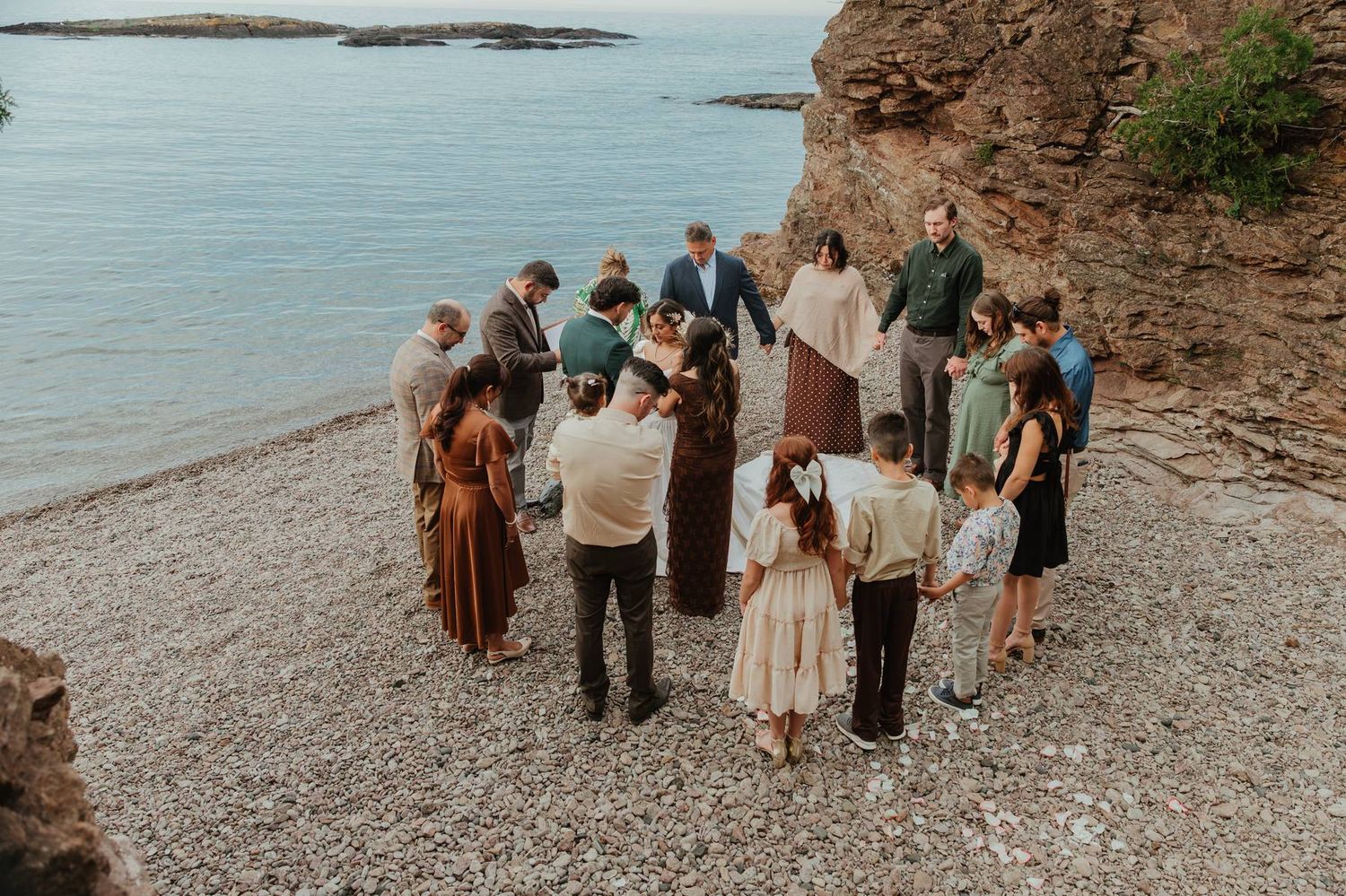 Small wedding ceremony on a rocky beach shore with guests gathered in a circle near ocean cliffs.