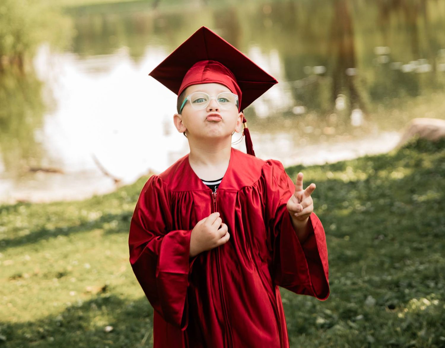Graduate in bright red cap and gown looking upward with joy in an outdoor park setting.