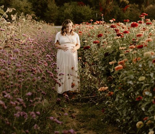 A white dress-clad figure stands in a garden path bordered by red poppies and purple flowers.